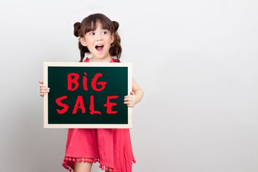 big sale discount for item in shopping mall promotion on end of year concept : adorable girl act surprise face holding chalk sign board with text big sale in red. copy space for your text