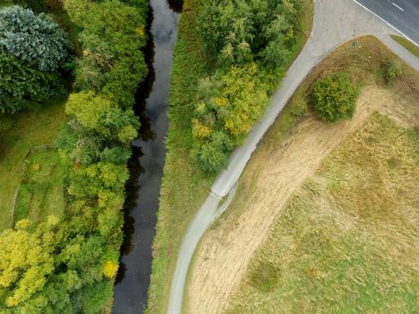 Abstract aerial view of a straightened stream next to a meadow with a large, isolated green tree, made by drone