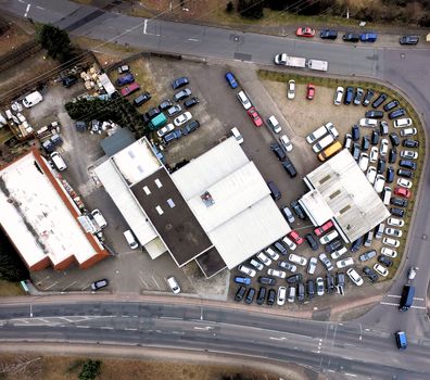 Aerial view of an industrial estate with many parking cars between two roads at the edge of a city, drones shot