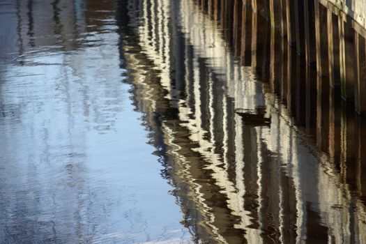 Water reflections of the sheet piling and commercial buildings in a quiet flowing river , Aller in Gifhorn, Germany