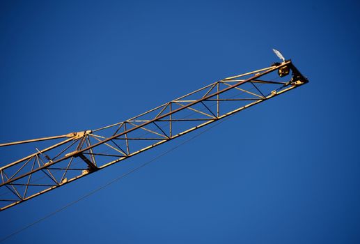 Front part of a large crane of a construction site in front of a bright blue sky, abstract