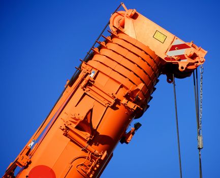 Zoom shot of an orange-coloured truck-mounted crane with telescopic boom pushed together, blue sky
