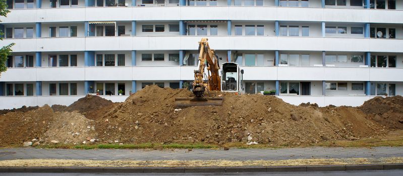 Construction site for the laying of new canals and pipes in front of a large, ugly apartment building with lots of cheap apartments, construct