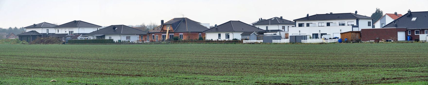 Panorama of a new housing estate with single-family houses on the edge of a village with arable land, lots of space and width as a header for a website, stitched