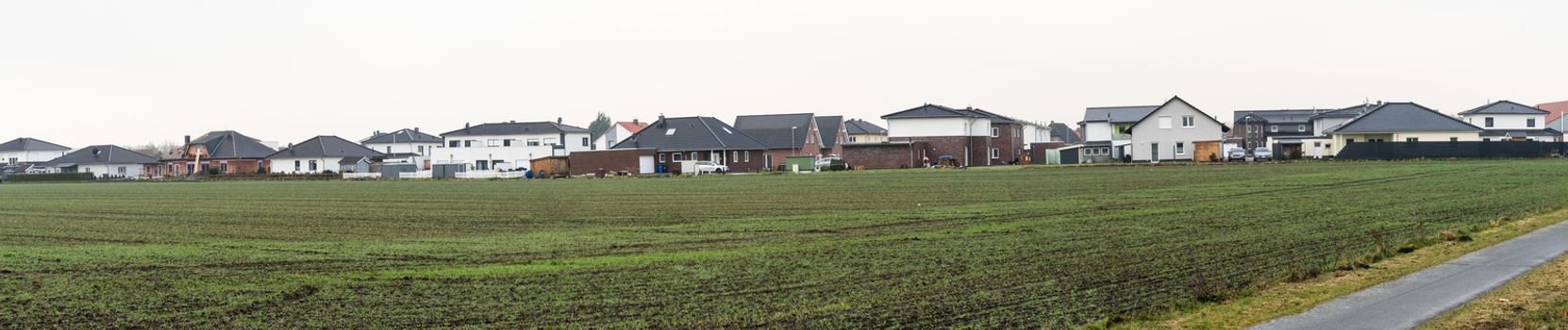 Panorama of a new housing estate with single-family houses on the edge of a village with arable land, lots of space and width as a header for a website, stitched