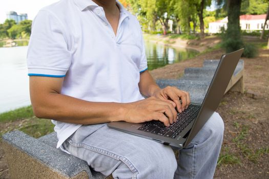 A man is typing on a laptop keyboard works in the park concept Workspace anyware and Remote online work 
