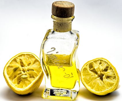 Bottle with lemon oil and two squeezed lemon halves against a white background, isolated