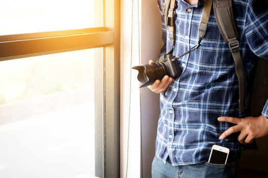 travel and photography concept. photographer with backpack and digital camera standing near window ready to travel for take photo , anonymous face. film effect