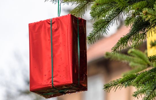 Red wrapped Christmas present with a green ribbon hanging on a Christmas tree