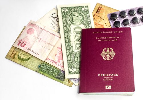 Preparing for a trip around the world with a passport, banknotes from the USA, Uganda, England, Turkey and Jordan as well as a package of charcoal tablets for stomach ailments and diarrhea, white background