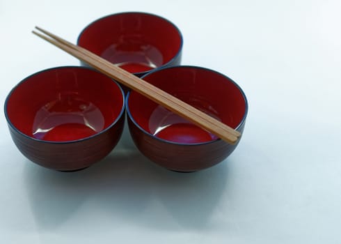 Three Japanese lacquer bowls and wooden chopsticks in front of a white background, isolated