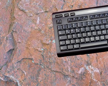 Computer keyboard of a computer in front of a background from a raw red sandstone plate, isolated, photomontage
