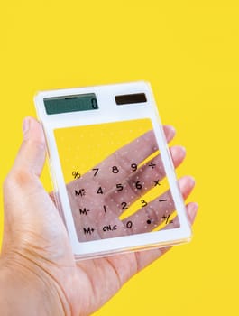 Hand showing digital calculator on yellow background.