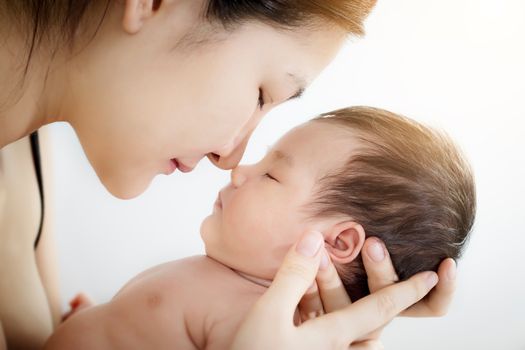 Concept of love and family relationship : Portrait of happy Asian mother use nose touch newborn cute little baby nose on a white bed at home. Parent and little kid relaxing hug and kiss at home.