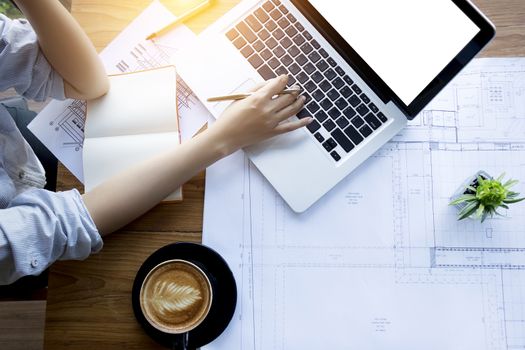 architect , engineering , creative and designer workspace concept : Top view of Asian female architect working with blueprint , notebook and laptop on architectural project , anonymous face.