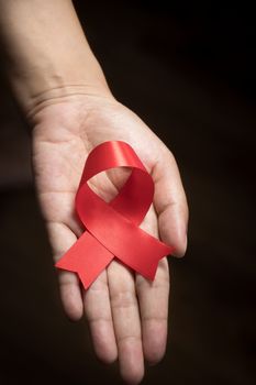 World AIDS Day concept : Red ribbon on human hand isolate on black background. Red ribbon symbolic bow color raising awareness on World AIDS Day , 1 December