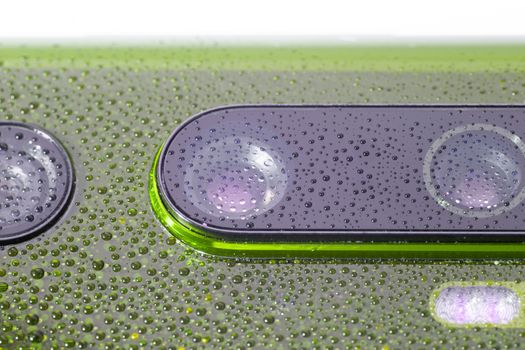 green phone camera lens covered with small water drops - close-up with selective focus and blur.