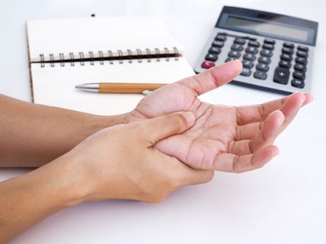 close up of hand of adult Thai Asian people with palm pain, Hand ache and wrist pain from work with notebooks, pen and calculator on table.