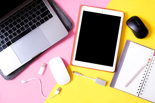 Top view working equipment with Laptop computers, tablets, notebook, pen and wireless mouse on pink and yellow color background.