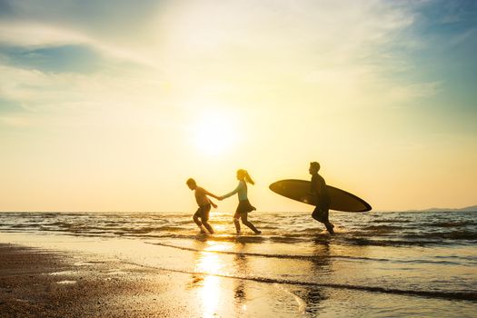 Outdoor sport activity friendship concept : Silhouette of group of young joyful surfer friend running into the sea with surf boards on sunset beach