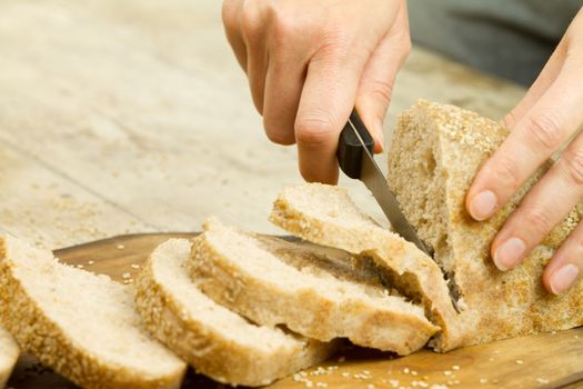 Close up of woman hands slicing a loaf of homemade bread with se