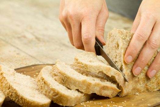 Close up of woman hands slicing a loaf of homemade bread with se