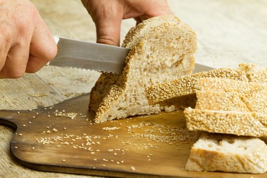 Close up of man hands slicing a loaf of homemade bread with sesa