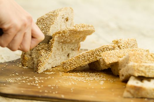 Close up of woman hands slicing a loaf of homemade bread with se