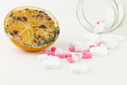 Concept: human GMO manipulation of nature and relative poisoned fruits. Close-up of an half orange contaminated by changing color from the medicines in front of it on a white background