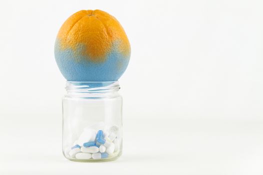 Concept: manipulation of human GMO of nature and related poisoned fruits. Close-up of a glass jar with a contaminated orange changing color from the medicines in the jar on a white background