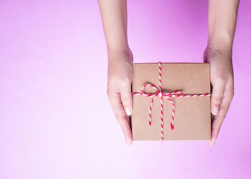 Girl's hands holding the simply package box as a present for Christmas, new year, valentine day or anniversary on pink background, top view