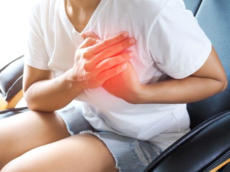 Asian women use hands to hold breasts due to myocardial infarction, symptoms of heart disease, Chest pain medical symptom and healthcare concept.