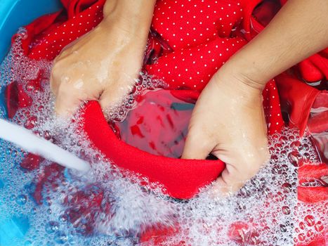 person washing clothes with hands using detergents, soak red fabric, t-shirt in laundry detergent