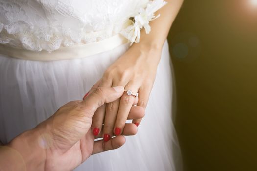 Wedding love couple concept : groom put wedding rings on bride finger on wedding day event, sunrise effect with lens flare
