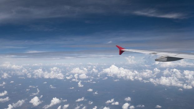 Plane travel concept : View from aircraft window. Clouds and blue sky under airplane wing as seen through window of an airplane in wide angel with copy space for travel agency background
