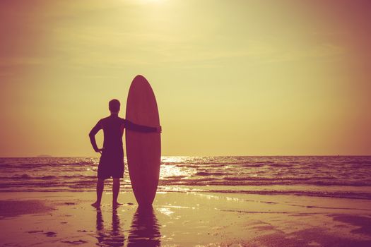Silhouette of surf man stand with a surfboard. Surfing at sunset beach. Outdoor water sport adventure lifestyle.Summer activity. Handsome Asia male model in his 20s.