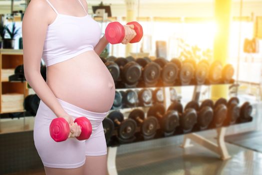 Pregnant exercises concept.A portrait of a Beautiful asian pregnant woman doing light exercise by using dumbbell with fitness background. Beautiful Asia female model in her 20s