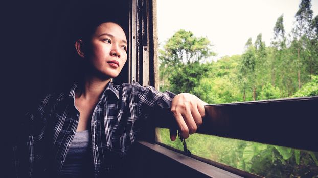 Backpacker tired from travel transportation. Young pretty Asia woman traveling to countryside by Thailand classic train sitting near the window. vintage filter. Beautiful Asian female model in her 20s