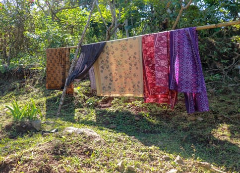 Sarong or Sarung is a traditional outfit worn by Hindus in Bali Island during ceremonies. Colored fabrics draped over the bamboo trunk are dried in the sun. Suspended washed laundry.