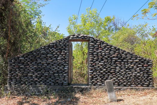 Stone wall with closed old wooden door by the road. A wall of pebbles in the jungle. Stones from the river that the water worked into smooth.