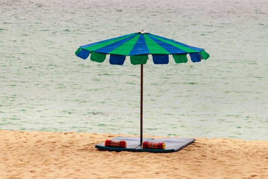 Beautiful sandy beach with umbrella, mattress and pillow