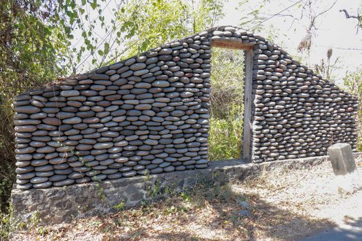 Stone wall with closed old wooden door by the road. A wall of pebbles in the jungle. Stones from the river that the water worked into smooth.