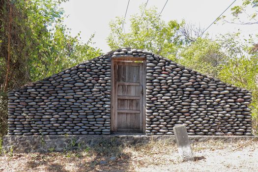 Stone wall with closed old wooden door by the road. A wall of pebbles in the jungle. Stones from the river that the water worked into smooth.