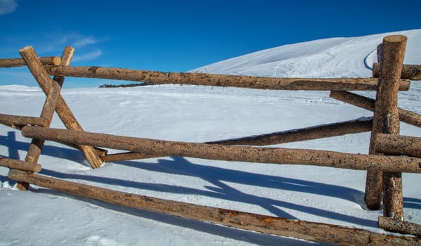 A large fence made of wooden logs, sits on a snow covered mountain near Camp Hale in Colorado.