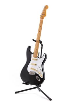 A vintage black and white electric guitar on a stand isolated on white