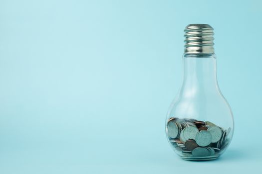 Coins in light bulb bottle shape on blue background with copy space for investment, business, finance and saving money concept