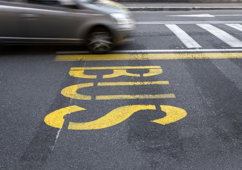 Yellow bus sign on the asphalt. Behind, a defocused car that passes in speed.