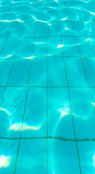 Sun reflection on the clear water ripples of swimming pool with tiles floor.