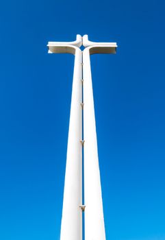 Modern iron cross of white color, isolated on a blue sky background.