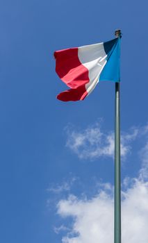 Flag of France, waving in the wind, on the blue sky background with white clouds.